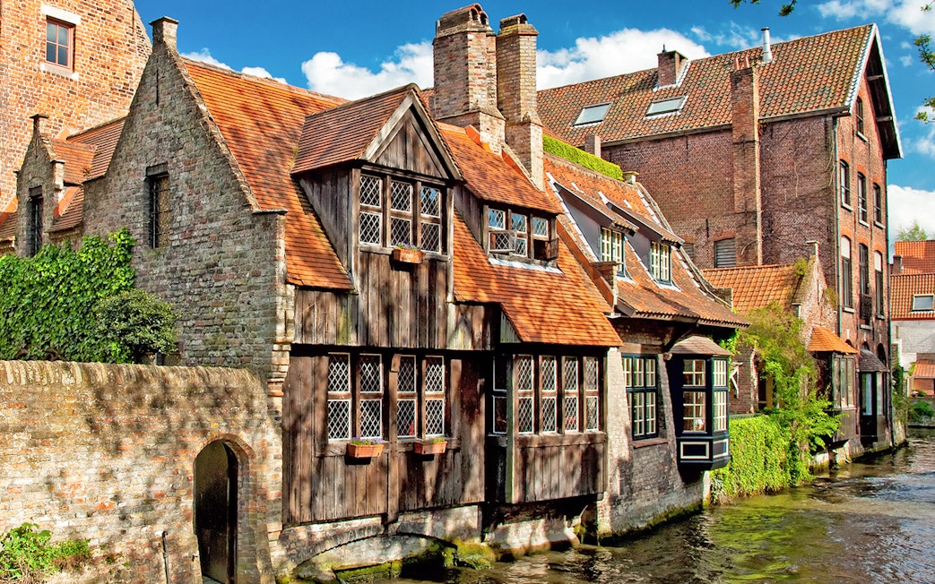 Historic canal-side buildings in Bruges, Belgium, with red-tiled roofs and ivy-covered walls.