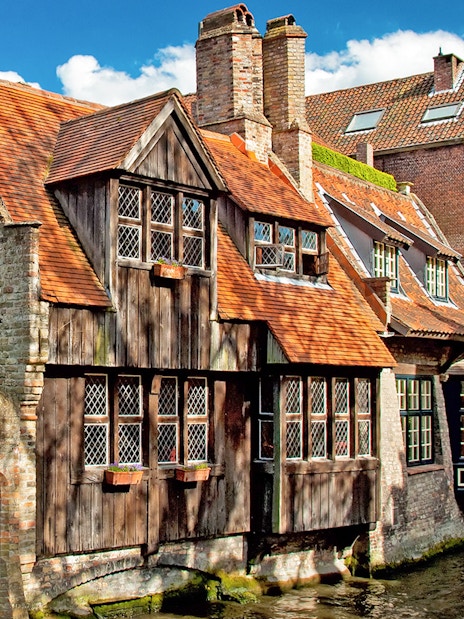 Historic canal-side buildings in Bruges, Belgium, with red-tiled roofs and ivy-covered walls.
