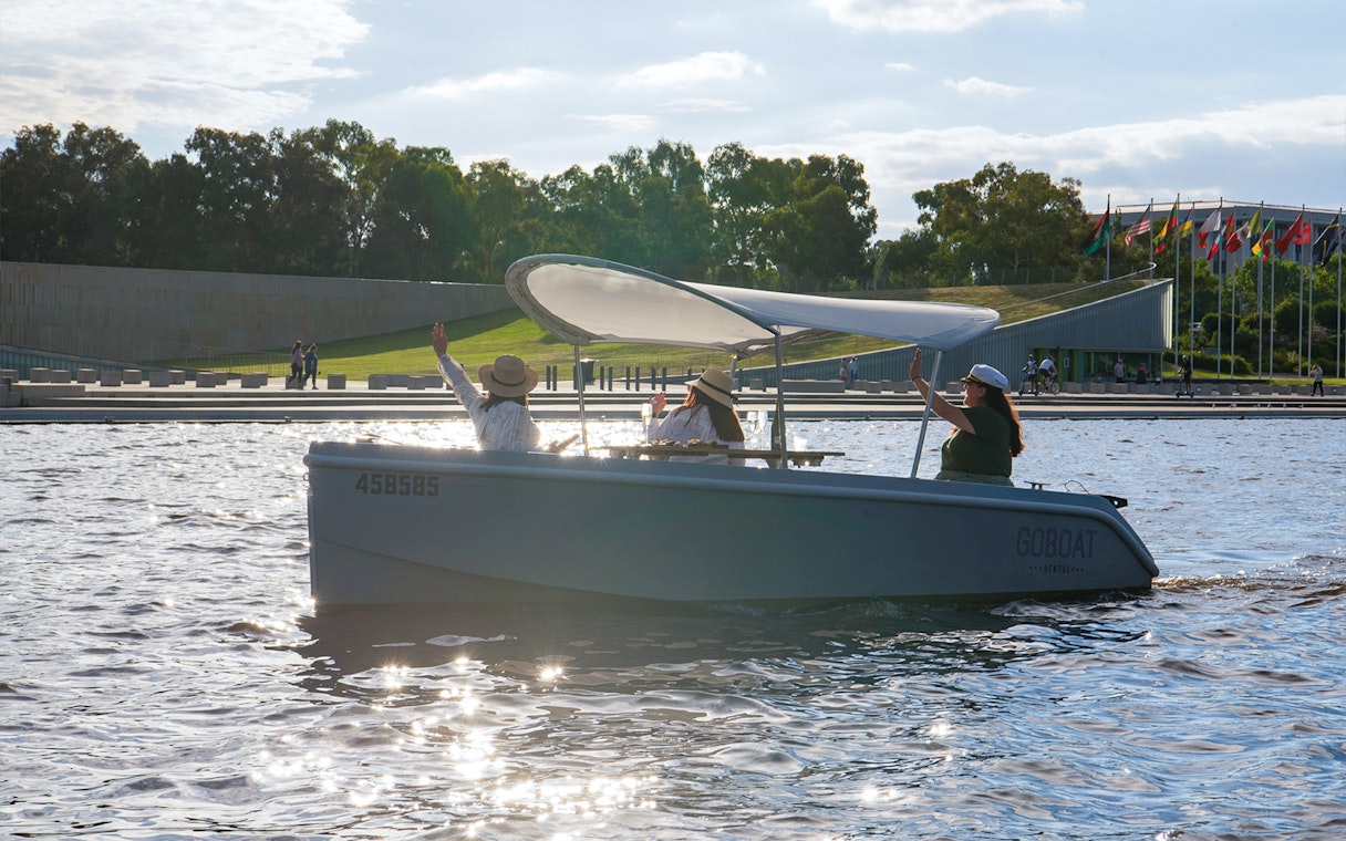 Electric picnic boat on Lake Burley Griffin, Canberra, with passengers waving.