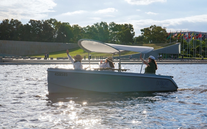 Electric picnic boat on Lake Burley Griffin, Canberra, with passengers waving.