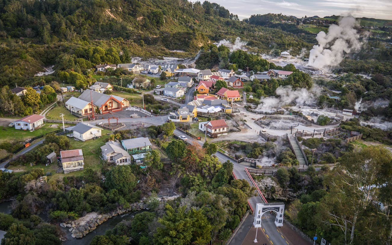 Aerial view of the Living Maori Village with geothermal steam vents and traditional buildings.