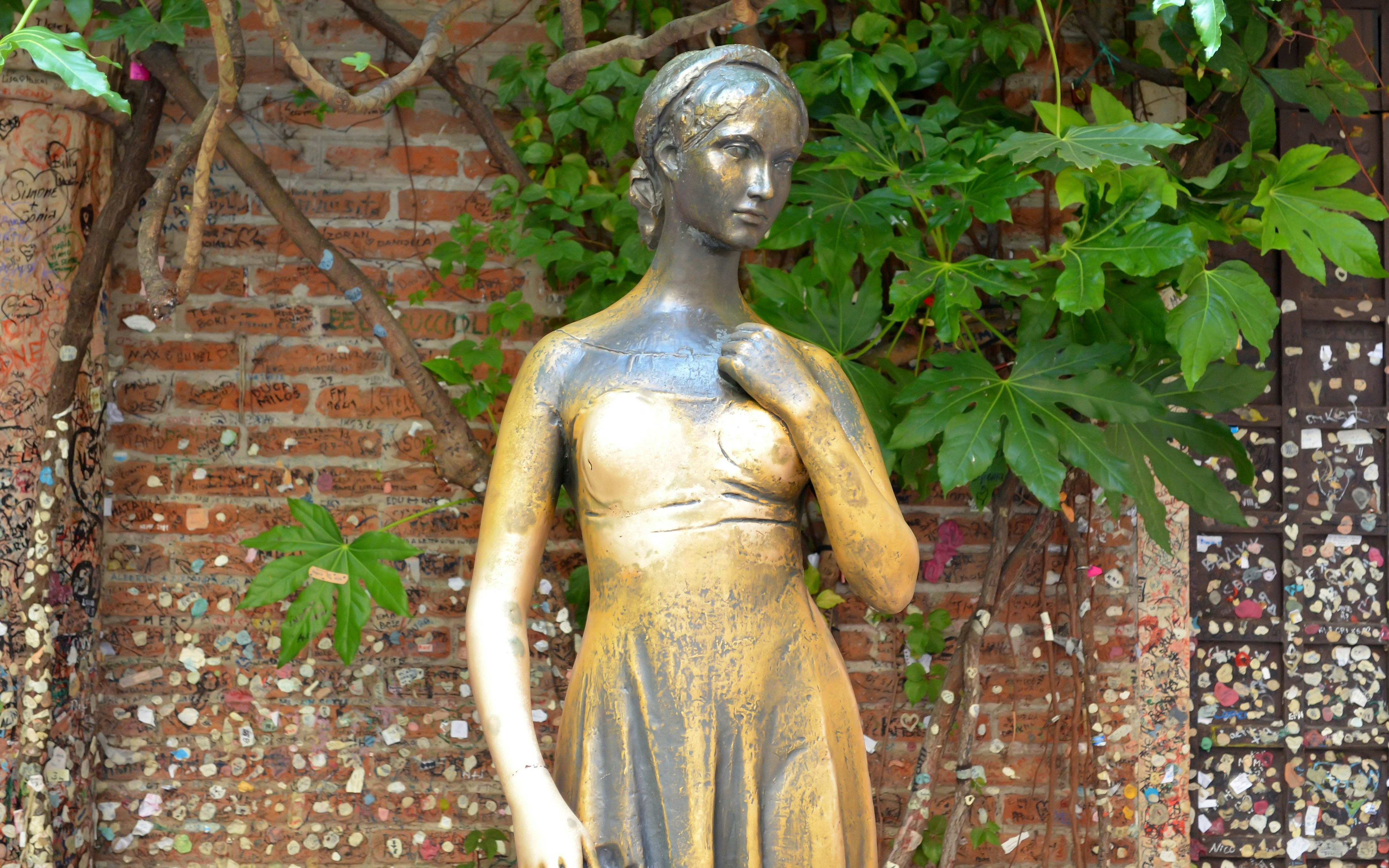 Juliet's bronze statue in Verona courtyard with love notes on brick wall.