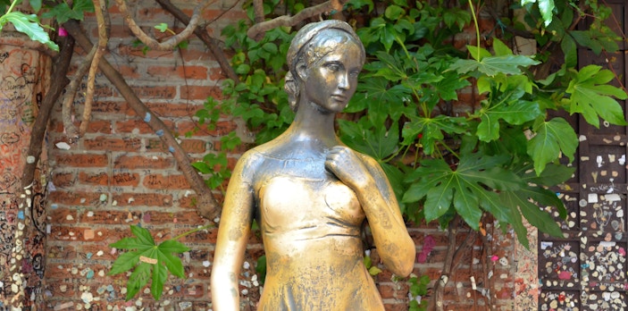 Juliet's bronze statue in Verona courtyard with love notes on brick wall.
