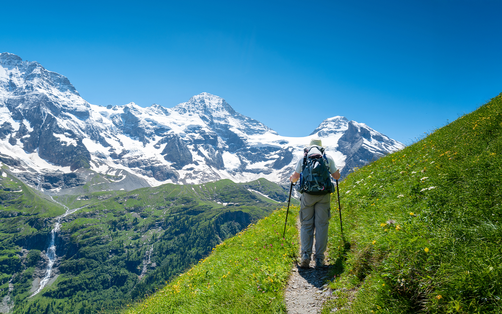 Man hiking in the Jungfrau region, Swiss Alps, Switzerland, with snow-capped peaks in the background.