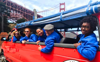 Tourists in a red open-top vehicle near Golden Gate Bridge, San Francisco.
