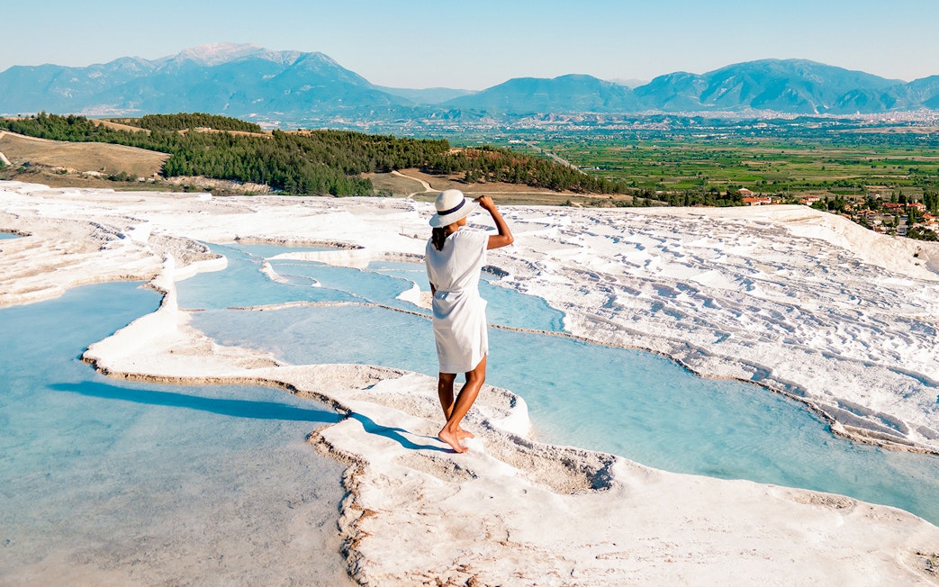 Person standing on Pamukkale's travertine terraces with mountain view, Antalya day trip.
