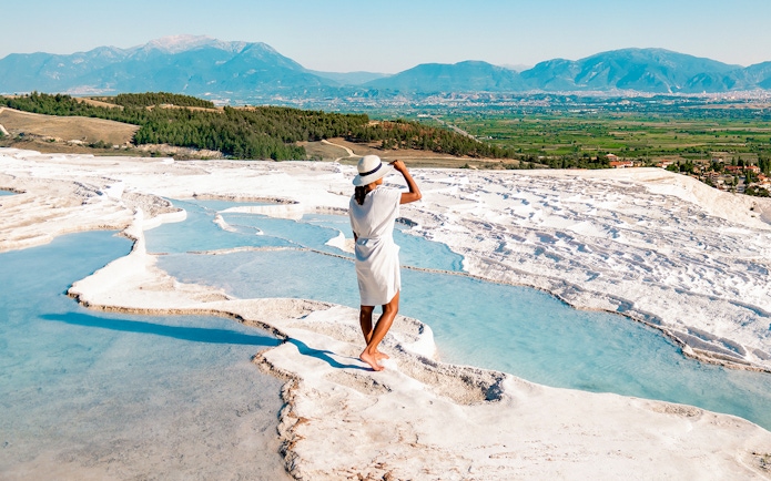 Person standing on Pamukkale's travertine terraces with mountain view, Antalya day trip.