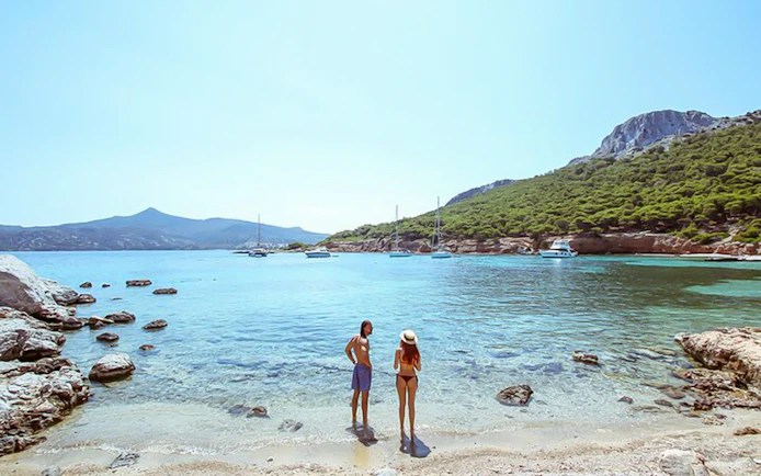 Guests enjoying the view on a beach during Athens Day Cruise with boats in the background.