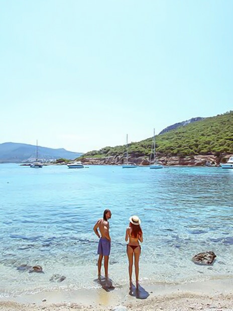 Guests enjoying the view on a beach during Athens Day Cruise with boats in the background.