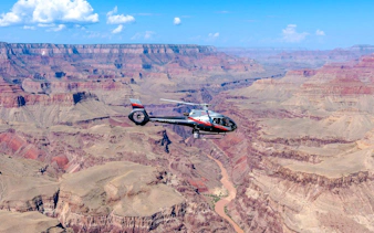 Helicopter flying over Grand Canyon South Rim with river below.