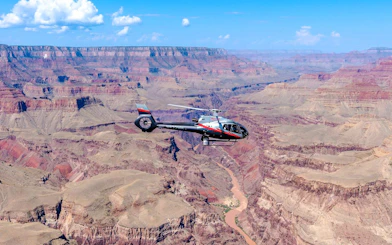 Helicopter flying over Grand Canyon South Rim with river below.