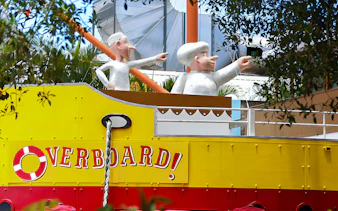 Figures on a yellow boat at The Ginger Factory, Australia, with "Overboard" sign.