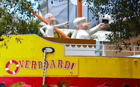 Figures on a yellow boat at The Ginger Factory, Australia, with "Overboard" sign.