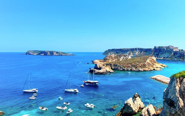 Sailboats near rocky coastline of Tremiti Islands on ferry route from Peschici.