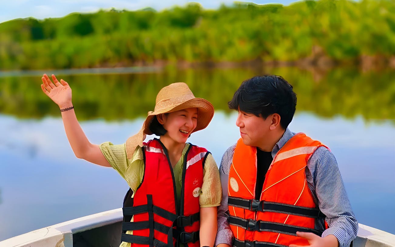 Couple enjoying Kawa Kawa River cruise in life jackets, surrounded by lush greenery.