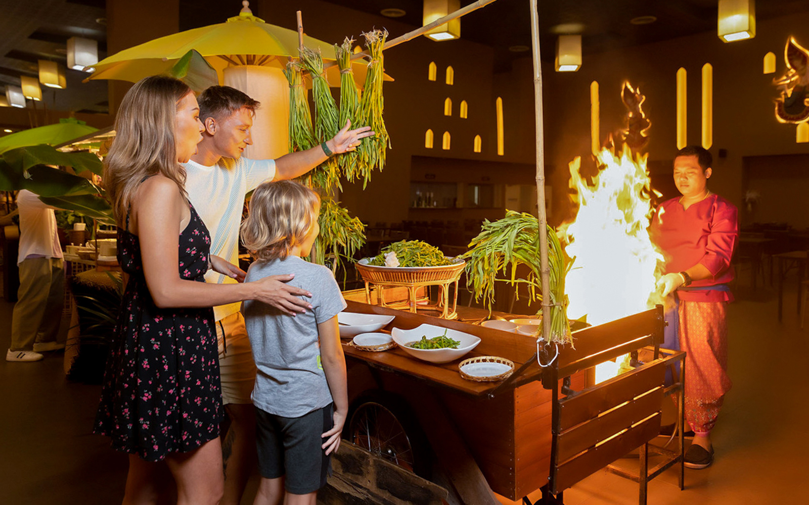 Family watching a live cooking demonstration with flames at Siam Niramit Phuket.