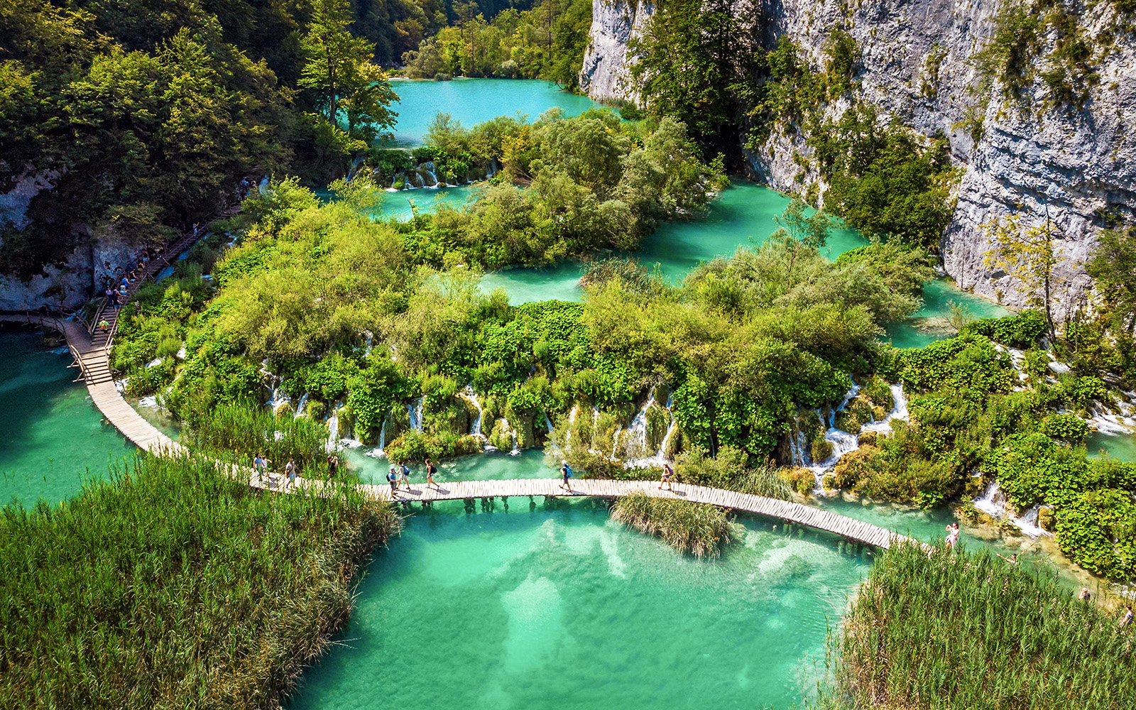 Visitors walking on a wooden path over turquoise lakes at Plitvice Lakes National Park, Croatia.