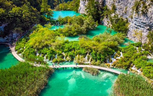 Visitors walking on a wooden path over turquoise lakes at Plitvice Lakes National Park, Croatia.