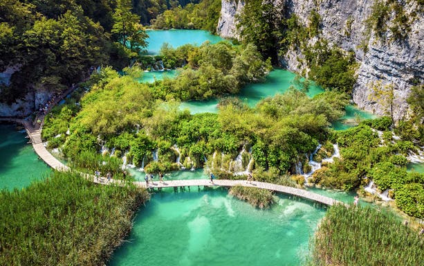 Visitors walking on a wooden path over turquoise lakes at Plitvice Lakes National Park, Croatia.
