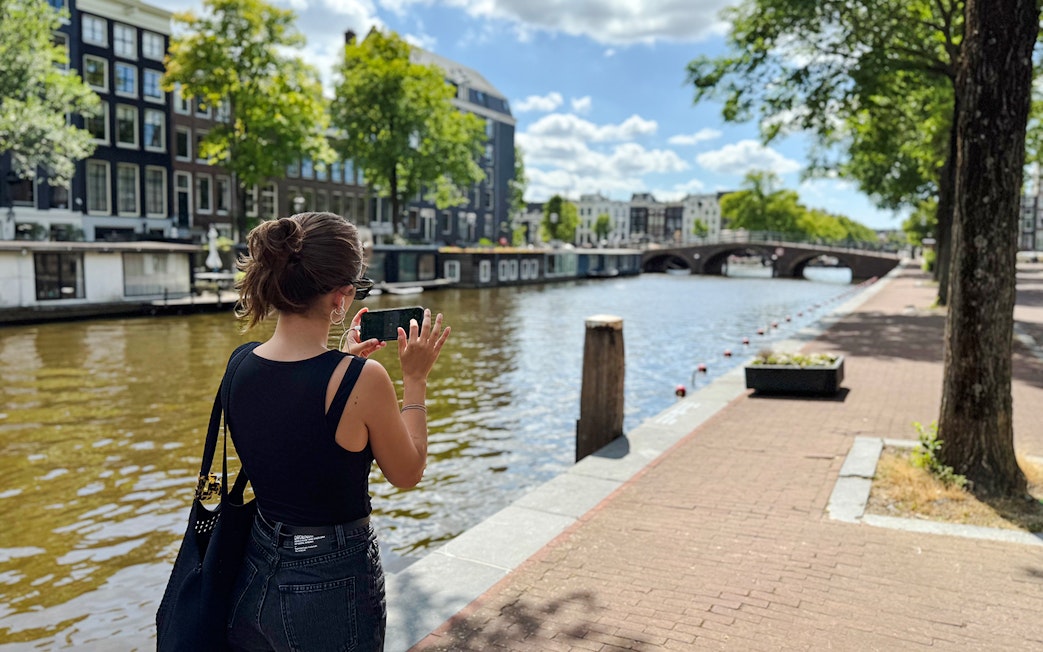 Guest using phone along Amsterdam canal during Anne Frank walk.