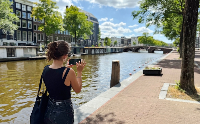 Guest using phone along Amsterdam canal during Anne Frank walk.
