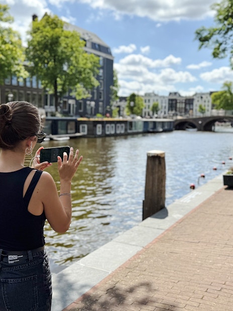 Guest using phone along Amsterdam canal during Anne Frank walk.
