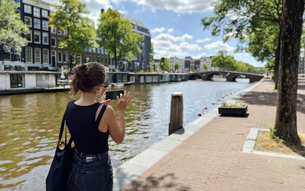Guest using phone along Amsterdam canal during Anne Frank walk.