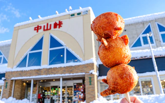 Skewered fried snacks in front of a snow-covered building in Sapporo, Hokkaido.