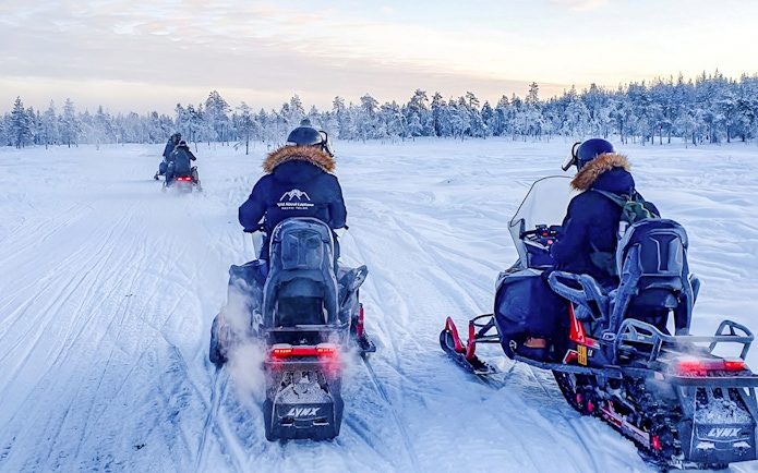Guests snowmobiling through snowy forest during Rovaniemi safari adventure.
