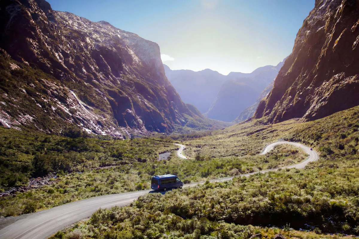 Milford Sound tour bus on winding road through scenic mountain landscape from Te Anau.