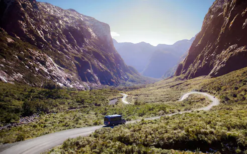 Milford Sound tour bus on winding road through scenic mountain landscape from Te Anau.