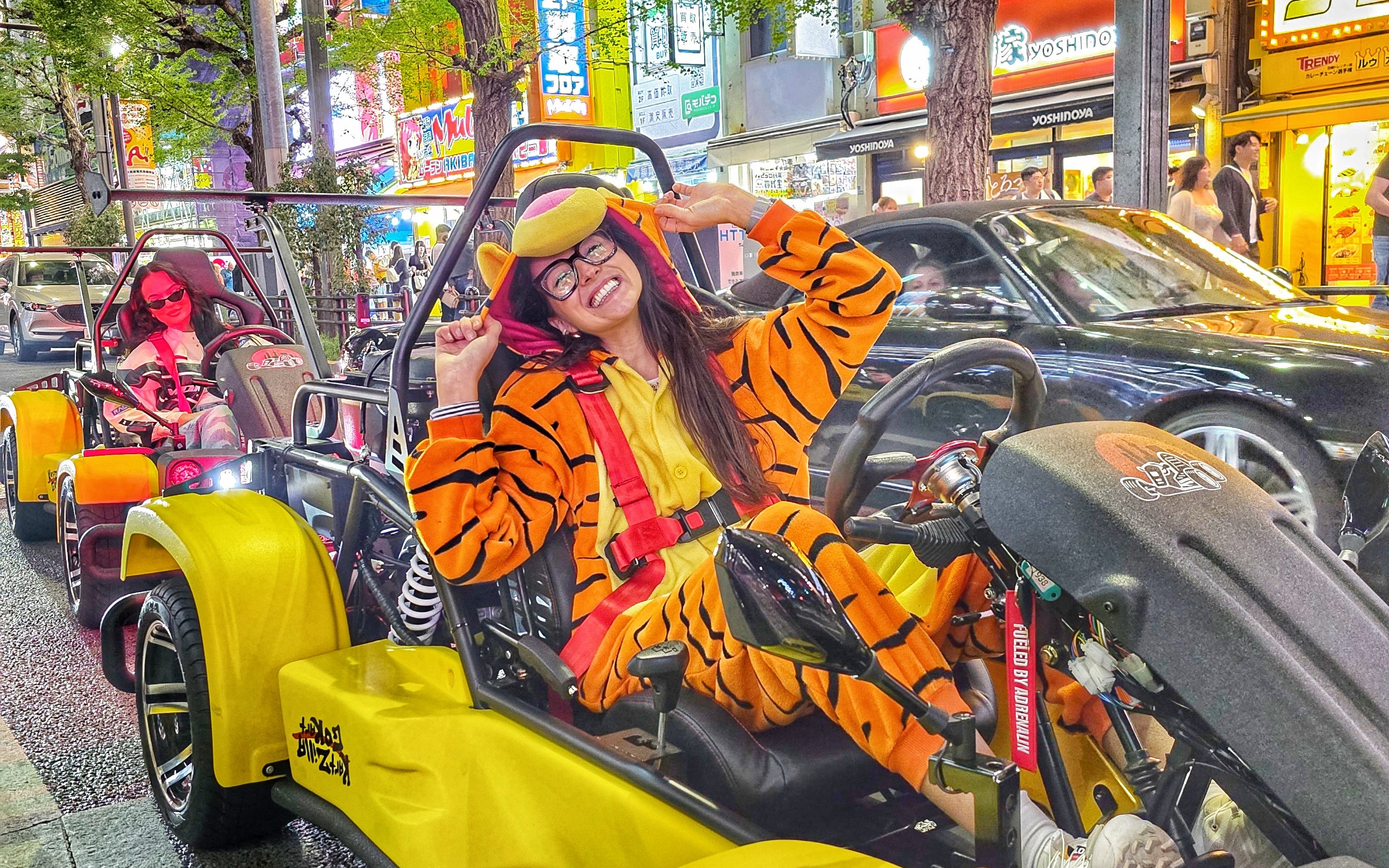 Go-kart riders in costume driving through Tokyo's vibrant old town streets at night.