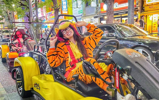 Go-kart riders in costume driving through Tokyo's vibrant old town streets at night.