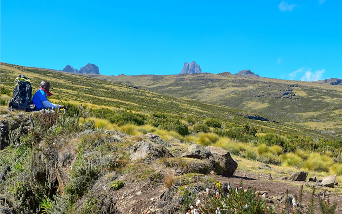 Hiker resting with backpack in Mount Kenya's volcanic landscape, Kenya.