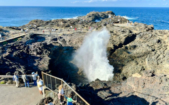 Kiama Blowhole with visitors watching water spout, rocky coastline, Sydney tour.