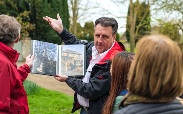 Tour guide showing photos to a group at Downton Abbey Village, Cotswolds.