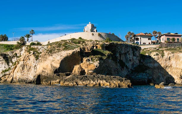 Cliffside view of Ortigia Island with historic buildings and sea caves.
