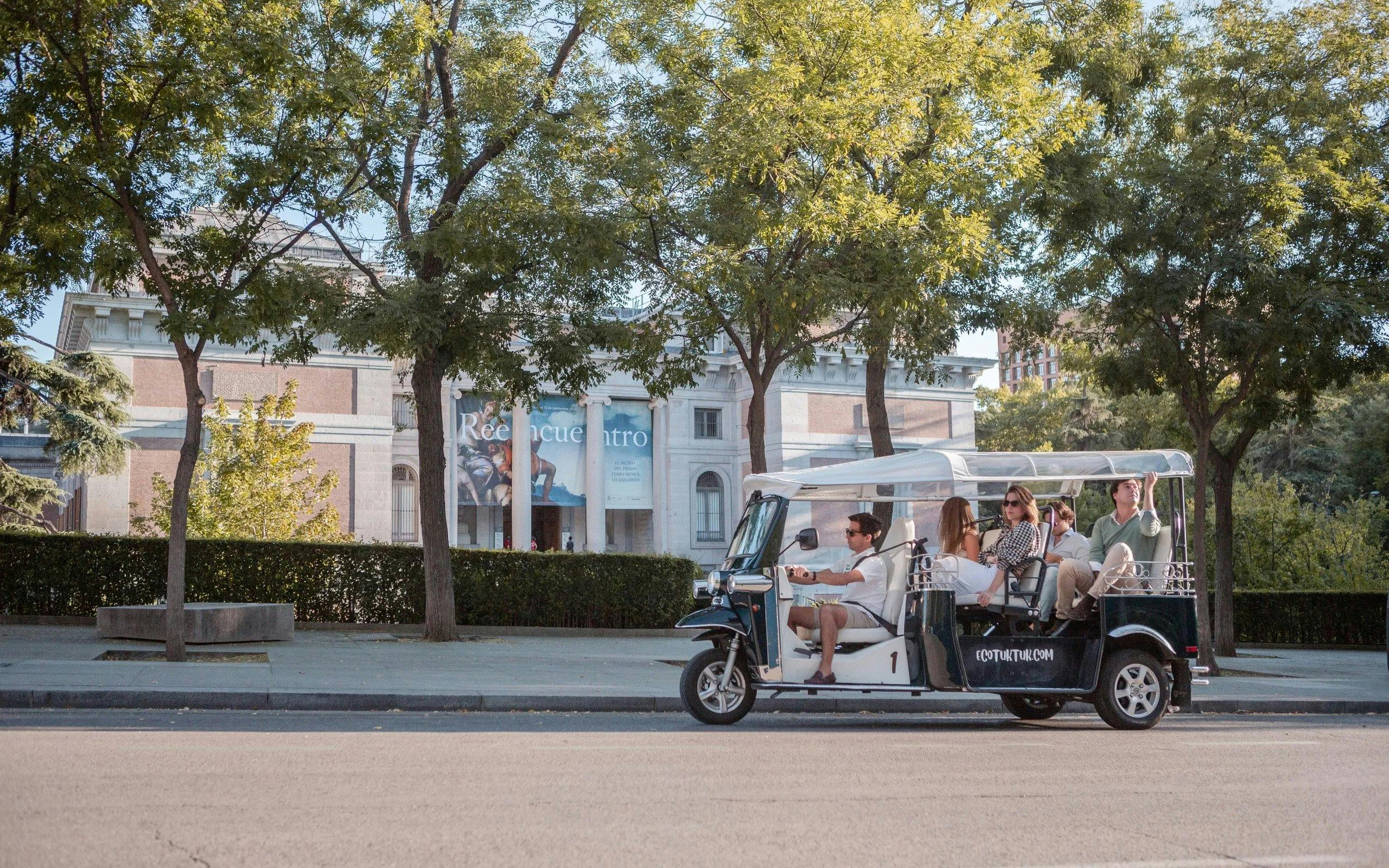 Tourists on an electric tuk-tuk tour in front of a museum in Madrid.