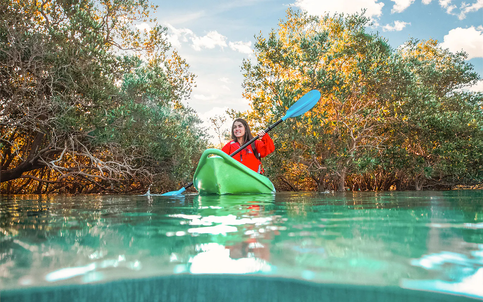 A kayaker paddles a green kayak through the mangroves of Abu Dhabi.