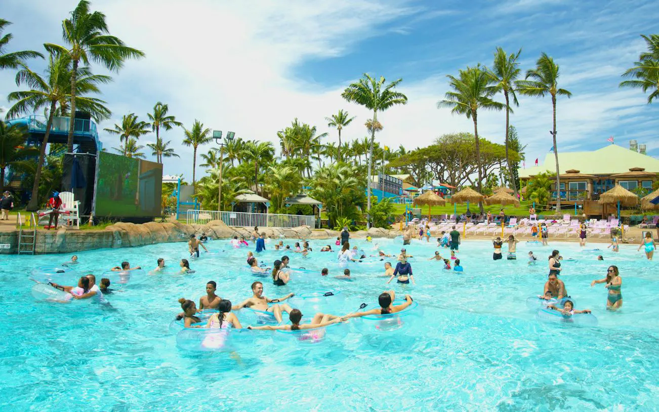 Visitors enjoying the wave pool at Wet 'n' Wild Hawaii, Oahu, surrounded by palm trees.