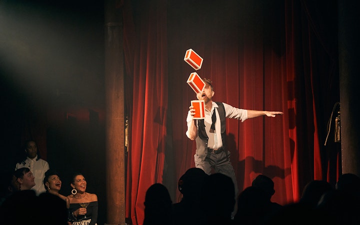 Performer juggling boxes on stage at Miss Behaves: Maverick's Variety Show.