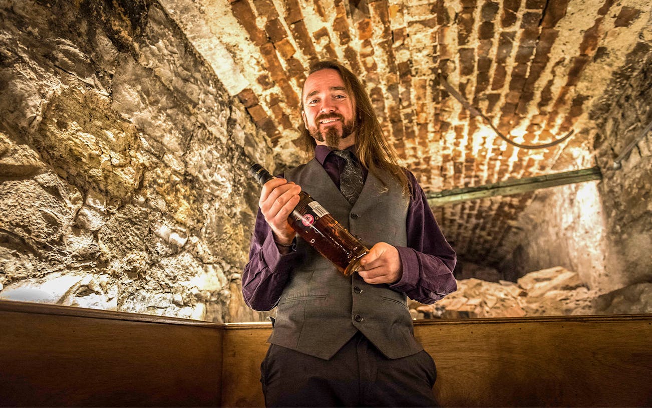 Whiskey expert holding a bottle in a stone cellar at Lost Close.