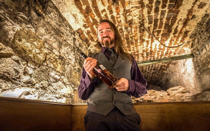 Whiskey expert holding a bottle in a stone cellar at Lost Close.