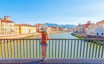 Traveler overlooking the Arno River in Pisa, Italy, with historic buildings in view.