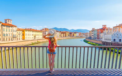 Traveler overlooking the Arno River in Pisa, Italy, with historic buildings in view.