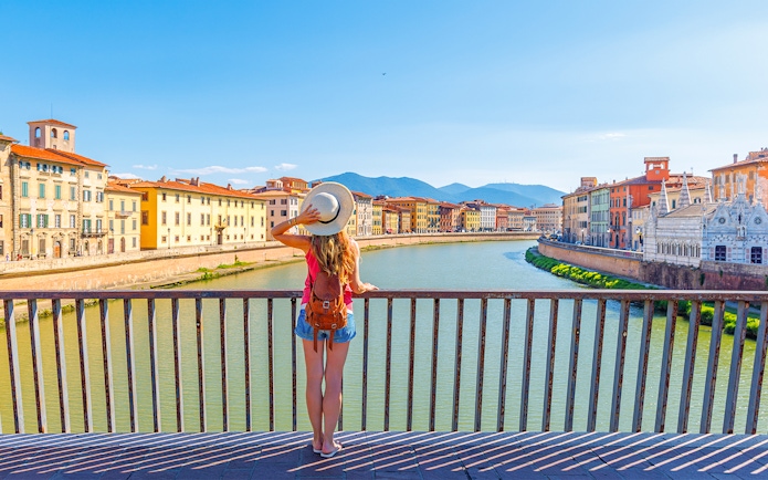 Traveler overlooking the Arno River in Pisa, Italy, with historic buildings in view.