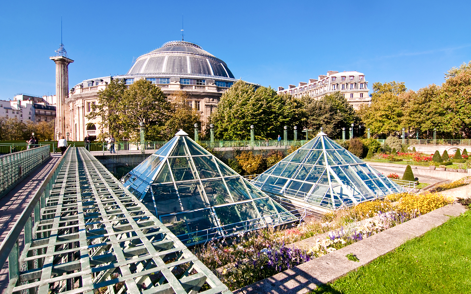 Glass pyramids and gardens at Jardin des Halles, Paris, with historic architecture in the background.