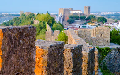 Ancient stone walls of Óbidos Castle with lush greenery, part of the self-guided tour from Lisbon.