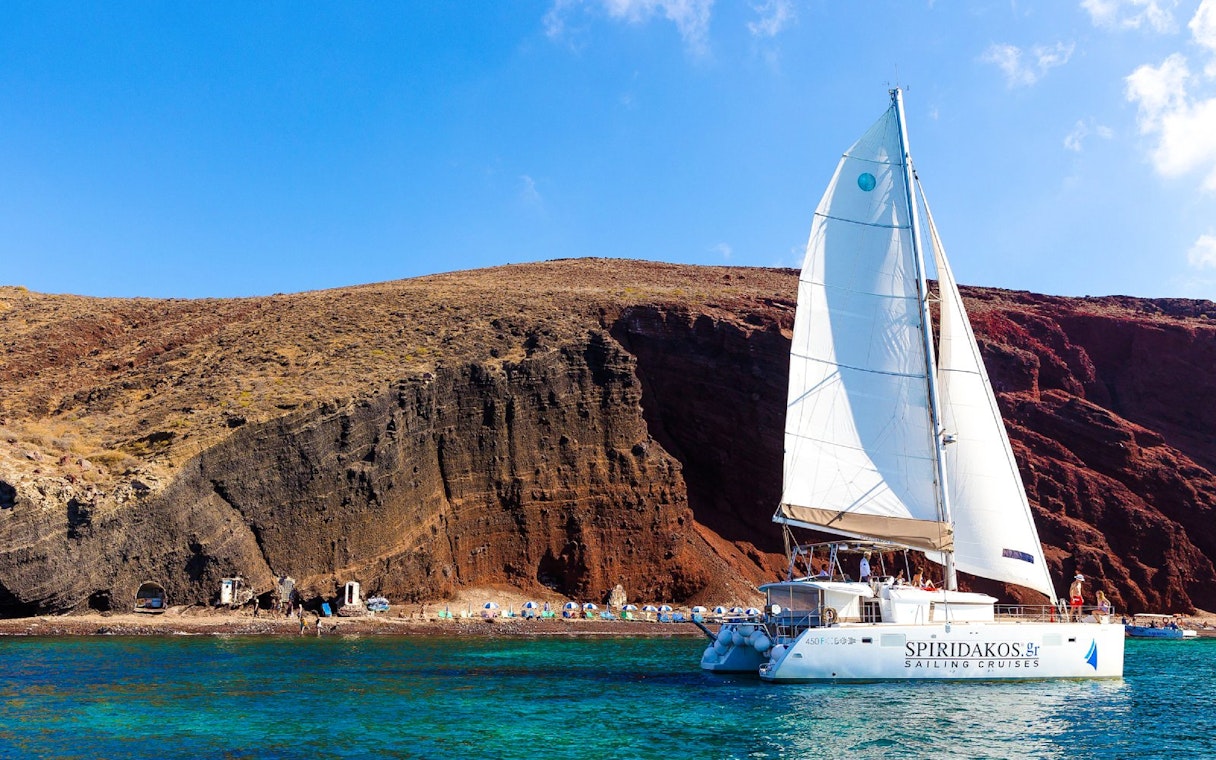 Catamaran sailing near the red cliffs of Santorini, Greece.