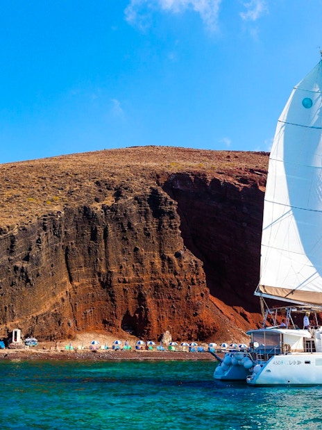 Catamaran sailing near the red cliffs of Santorini, Greece.